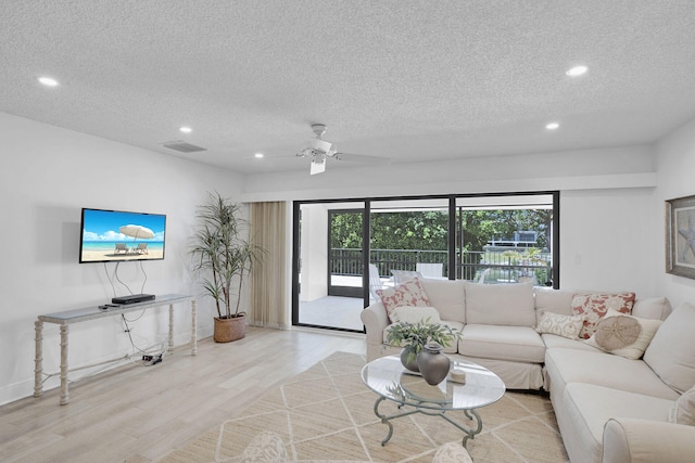 living room featuring ceiling fan, light hardwood / wood-style floors, and a textured ceiling