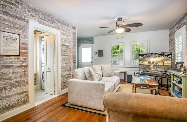 living room featuring stacked washer / dryer, brick wall, hardwood / wood-style floors, and ceiling fan