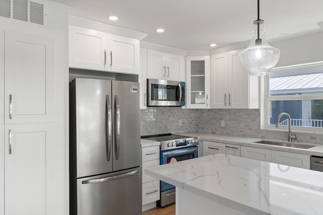 kitchen with sink, appliances with stainless steel finishes, light stone countertops, white cabinets, and decorative light fixtures