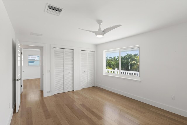 unfurnished bedroom with multiple closets, ceiling fan, and light hardwood / wood-style floors