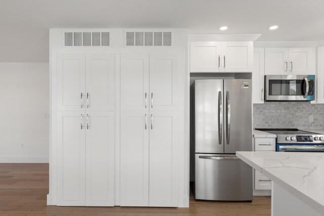 kitchen with appliances with stainless steel finishes, light stone counters, tasteful backsplash, light hardwood / wood-style floors, and white cabinets