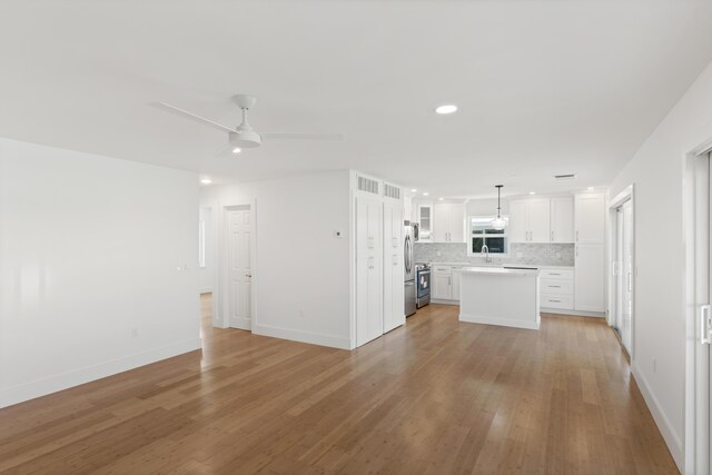 kitchen with appliances with stainless steel finishes, white cabinetry, backsplash, hanging light fixtures, and a center island