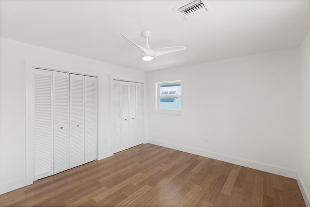 unfurnished bedroom with ceiling fan, wood-type flooring, and multiple closets