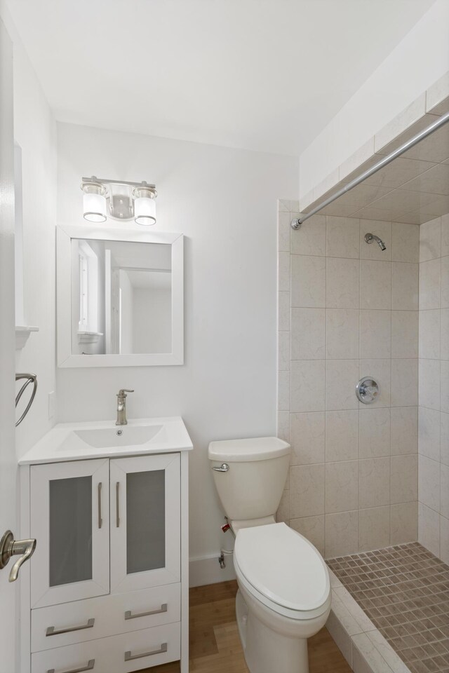 bathroom with hardwood / wood-style flooring, vanity, toilet, and a tile shower