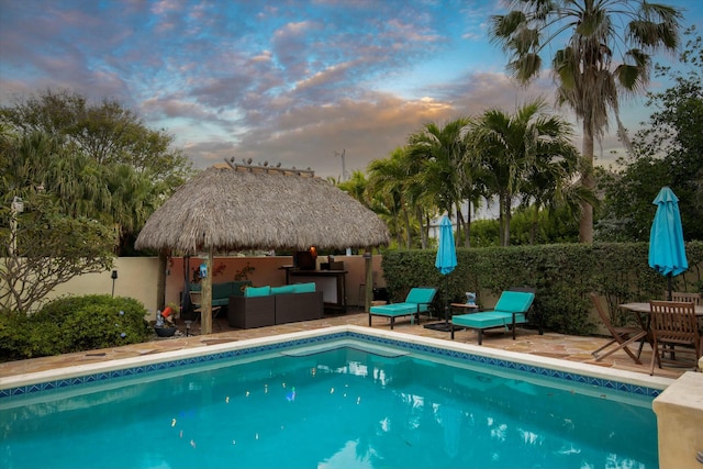 pool at dusk with a gazebo, an outdoor hangout area, and a patio area