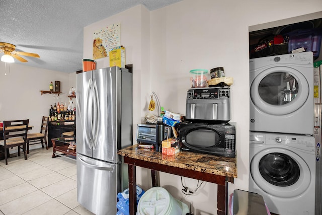 laundry room with stacked washing maching and dryer, light tile patterned floors, ceiling fan, and a textured ceiling