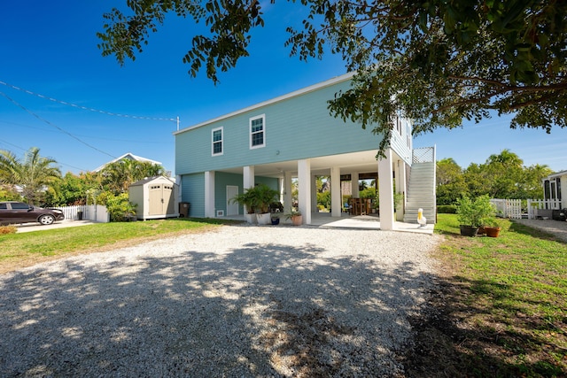 view of front of home with an outbuilding, fence, a carport, a shed, and gravel driveway