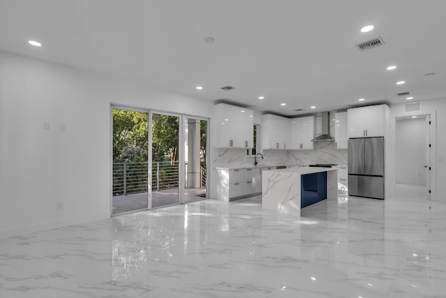 kitchen with sink, white cabinets, stainless steel fridge, a center island, and wall chimney range hood