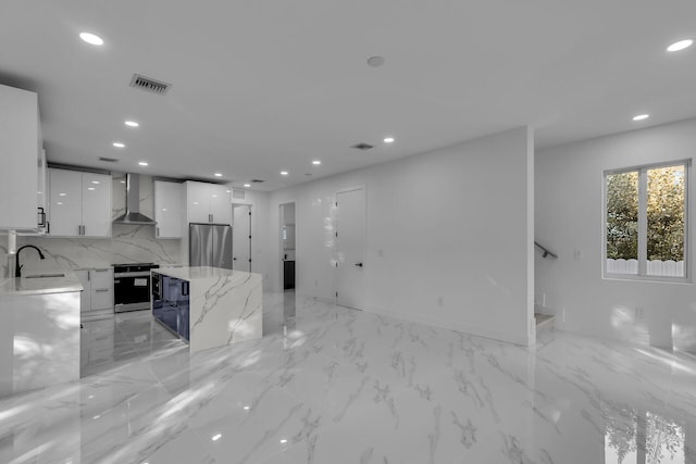 kitchen featuring sink, white cabinets, light stone counters, stainless steel appliances, and wall chimney exhaust hood