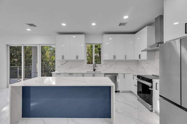 kitchen featuring sink, a center island, wall chimney range hood, stainless steel appliances, and white cabinets