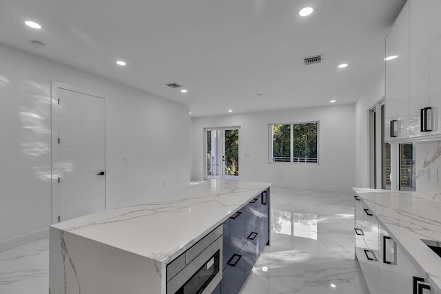 kitchen with light stone countertops, a kitchen island, stainless steel microwave, and white cabinets