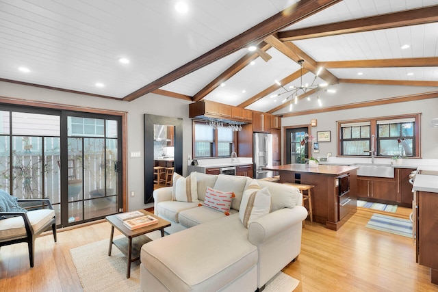 living room with lofted ceiling with beams, an inviting chandelier, sink, and light hardwood / wood-style flooring