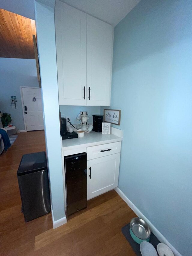 bar featuring dark hardwood / wood-style flooring, beverage cooler, and white cabinets