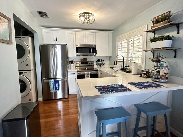 kitchen with stainless steel appliances, white cabinetry, stacked washer and dryer, and kitchen peninsula