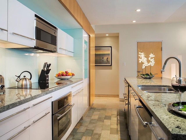 kitchen with white cabinetry, appliances with stainless steel finishes, sink, and light stone counters