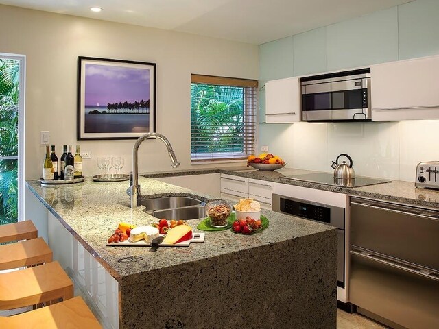 kitchen featuring white cabinetry, black electric stovetop, sink, and light stone counters