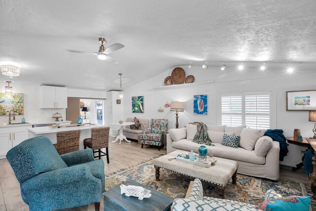 living room featuring vaulted ceiling, light hardwood / wood-style floors, sink, and a textured ceiling