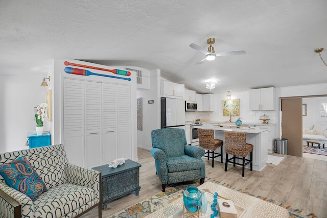 living room with lofted ceiling, sink, light hardwood / wood-style flooring, a textured ceiling, and ceiling fan