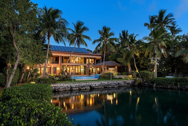 back house at dusk with a balcony, a water view, and solar panels