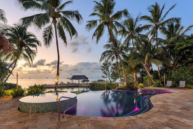 pool at dusk featuring a patio and a water view