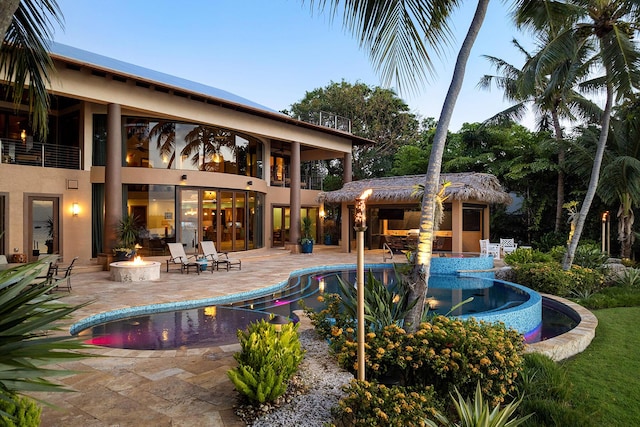 pool at dusk with an outdoor fire pit and a patio area