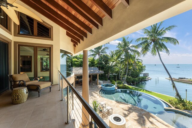 balcony with a patio area, an outdoor fire pit, an in ground hot tub, and a water view