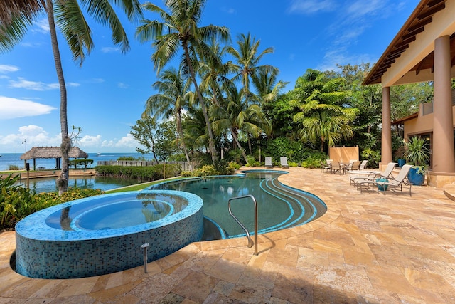 view of swimming pool featuring an in ground hot tub, a water view, and a patio