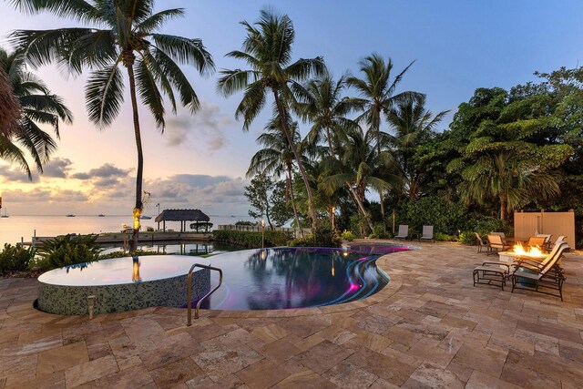 pool at dusk with a water view, a patio area, and an outdoor fire pit