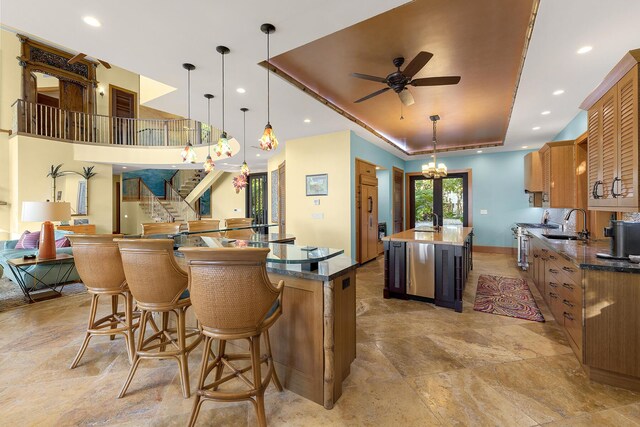 kitchen featuring ceiling fan with notable chandelier, decorative light fixtures, sink, a center island, and a tray ceiling