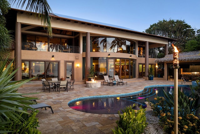 back house at dusk with a patio, a balcony, and an outdoor fire pit