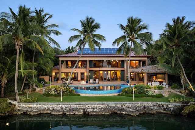 back house at dusk with solar panels, a patio area, a balcony, and a water view