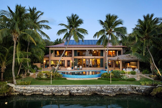 back house at dusk with solar panels, a patio area, a balcony, and a water view