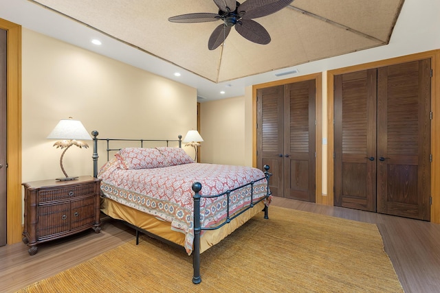 bedroom featuring hardwood / wood-style flooring, ceiling fan, and multiple closets