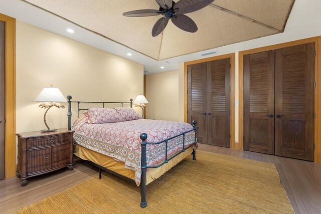 bedroom featuring hardwood / wood-style flooring, ceiling fan, and multiple closets