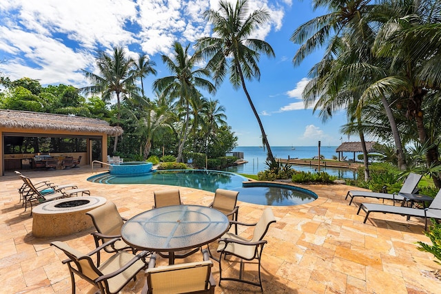 view of pool with a fire pit, area for grilling, an in ground hot tub, a water view, and a patio area