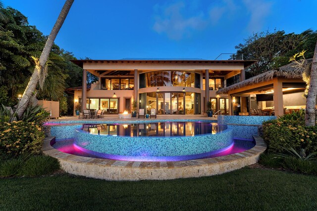 back house at dusk with a swimming pool with hot tub, a patio, and a balcony