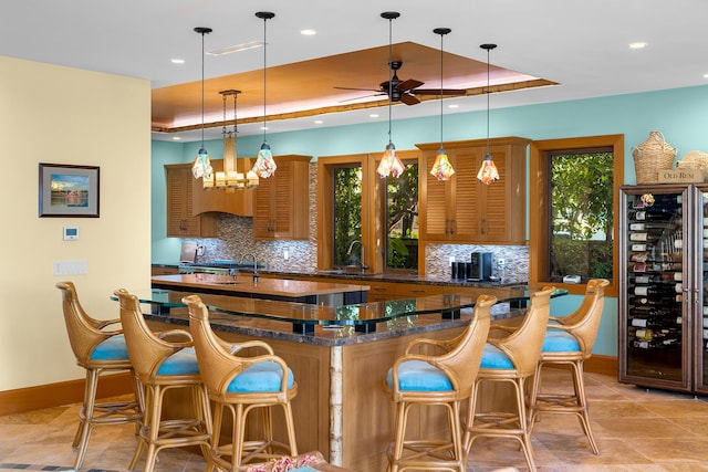 bar with hanging light fixtures, dark stone countertops, backsplash, and a tray ceiling