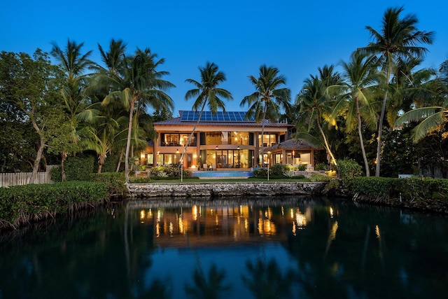 back of property with a water view, a balcony, and solar panels