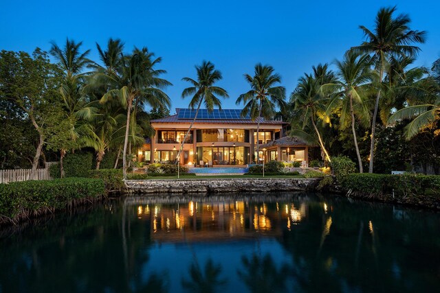 back of property with a water view, a balcony, and solar panels