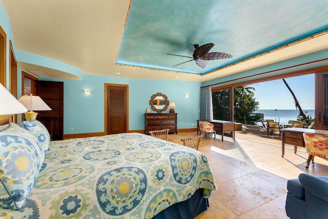 bedroom featuring a raised ceiling, a water view, access to outside, and ceiling fan