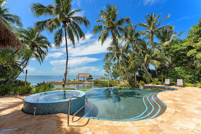 view of pool with an in ground hot tub, a water view, and a patio