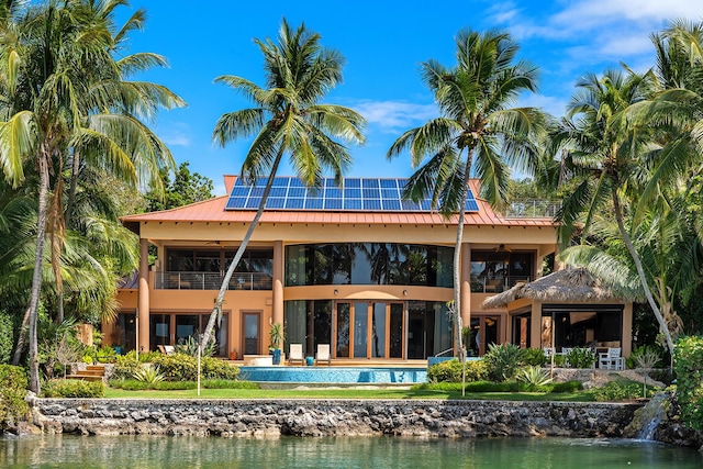 rear view of house featuring a water view, a balcony, and solar panels