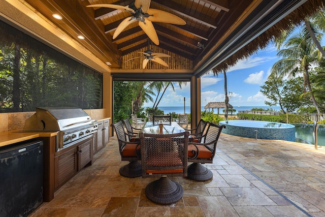 view of patio with grilling area, a water view, ceiling fan, and an outdoor kitchen