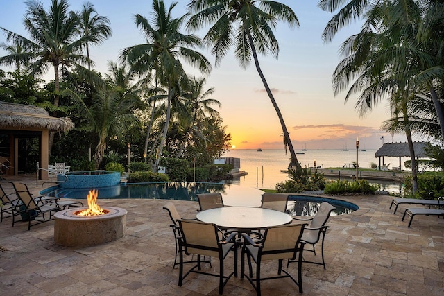 patio terrace at dusk with a swimming pool with hot tub, a water view, and a fire pit