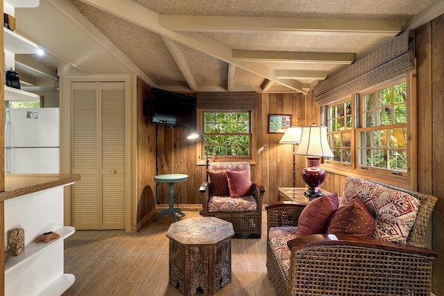 living room with beamed ceiling, wood-type flooring, a textured ceiling, and wooden walls