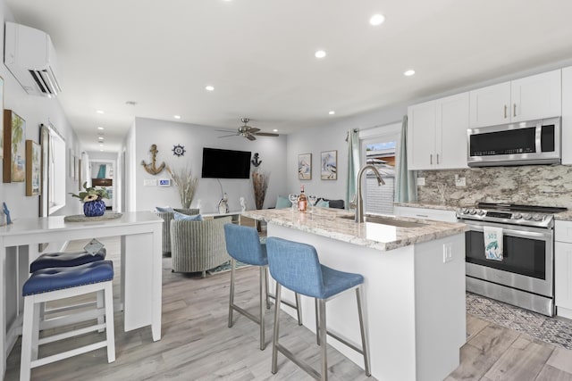 kitchen with an island with sink, a wall unit AC, open floor plan, stainless steel appliances, and a sink