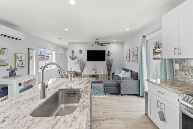 kitchen featuring light stone counters, a wall unit AC, a sink, white cabinets, and open floor plan