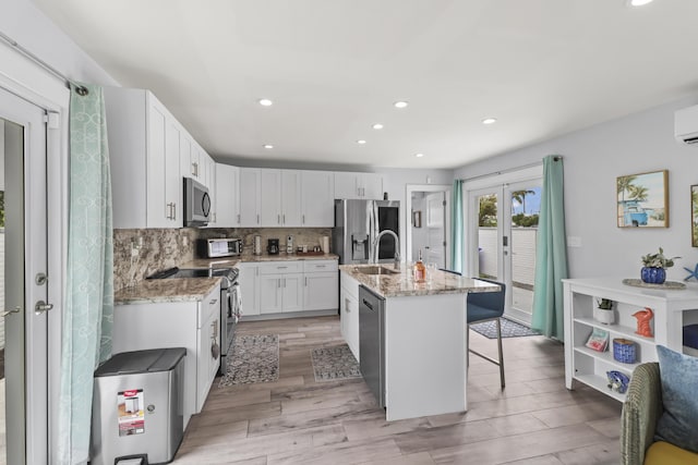 kitchen with a center island with sink, appliances with stainless steel finishes, white cabinets, a sink, and light stone countertops