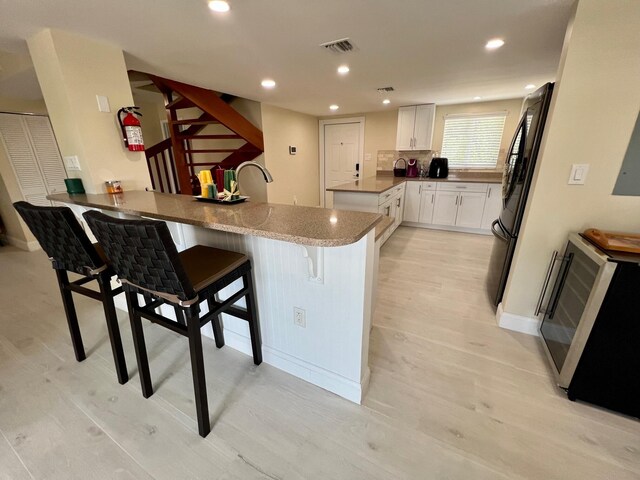 kitchen featuring white cabinetry, a kitchen breakfast bar, black fridge, kitchen peninsula, and light stone countertops