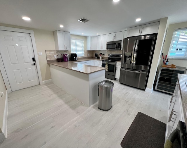 kitchen featuring appliances with stainless steel finishes, white cabinetry, decorative backsplash, kitchen peninsula, and light wood-type flooring